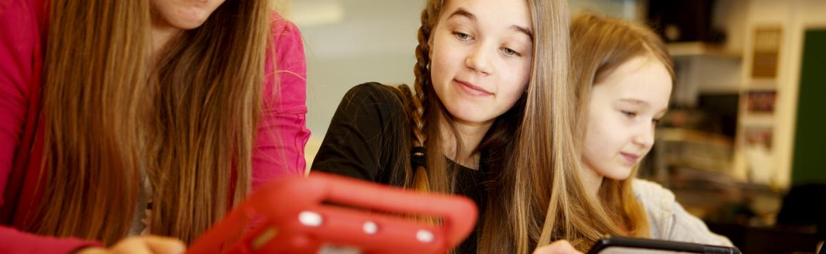 Kaksi alakouluikäistä tyttöä istuu luokassa vierekkäin tabletit käsissään. 