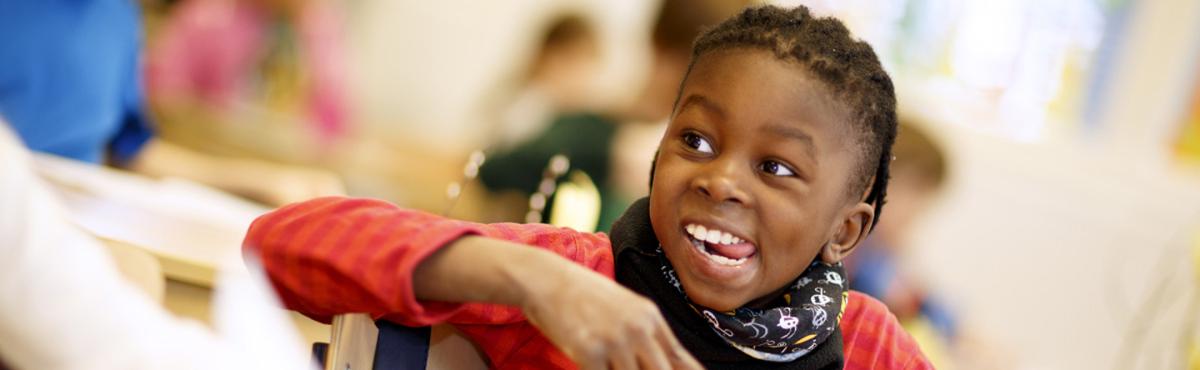 Iloinen pieni koululaispoika virnistää ja katsoo olkansa yli. 