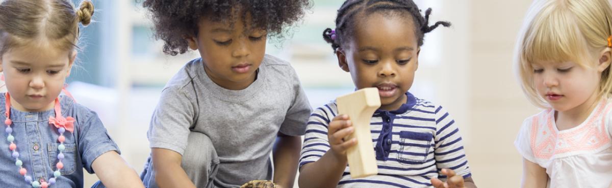 Neljä päiväkoti-ikäistä lasta leikkii keskittyneesti puisilla rakennuspalikoilla. 
