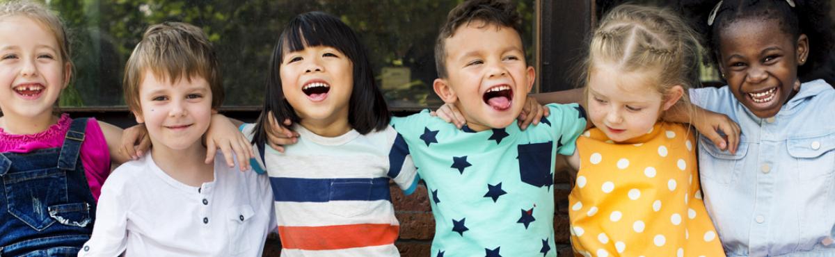 Kuusi alakouluikäistä lasta istuu vierekkäin kädet toistensa hartioilla. 