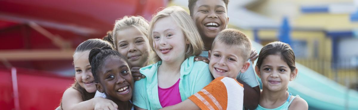 Joukko erilaisia lapsia halaa toisiaan ja katsoo nauraen sivuun kamerasta. 