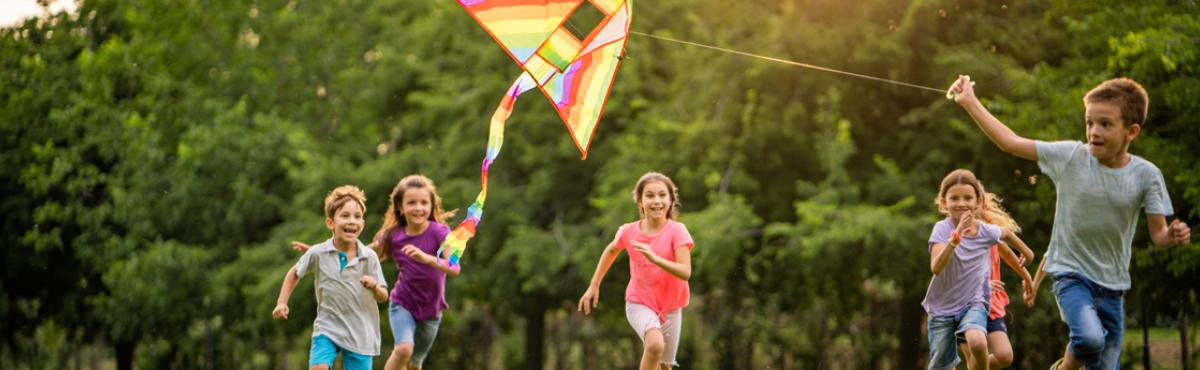 Poika juoksee leija kädessä niityllä. Hänen takanaan juoksee joukko muita lapsia. 