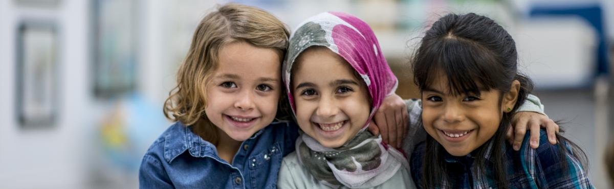 Kolme alakouluikäistä lasta kädet toistensa hartioille hymyilevät kameralle.