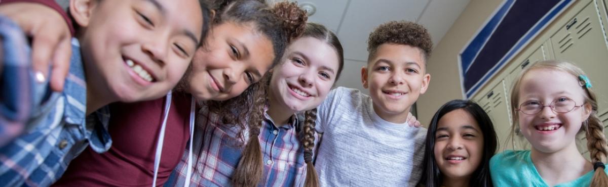 Kuusi lasta katsoo hymyillen kameraan kädet toistensa olkapäillä.