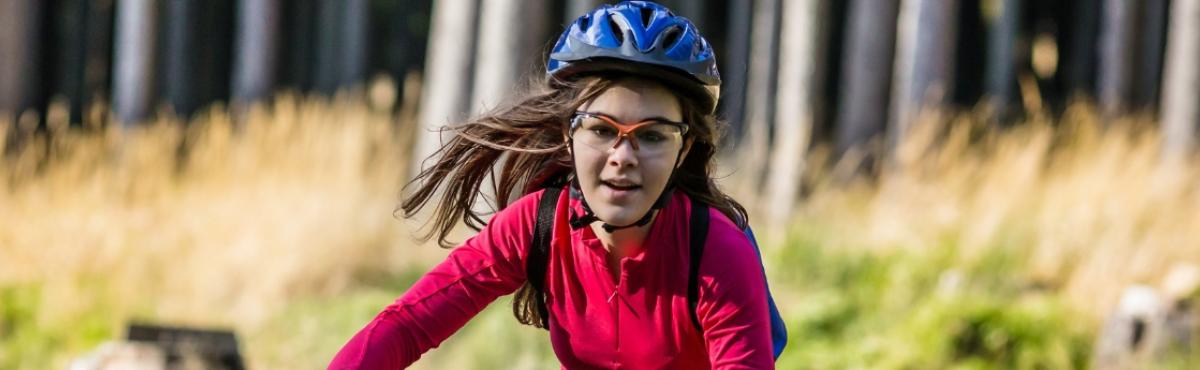 Punaiseen paitaan, suojalaseihin ja kypärään pukeutunut teini katsoo keskittyneesti eteensä pitkät hiukset liehuen. Taustalla näkyy metsää.